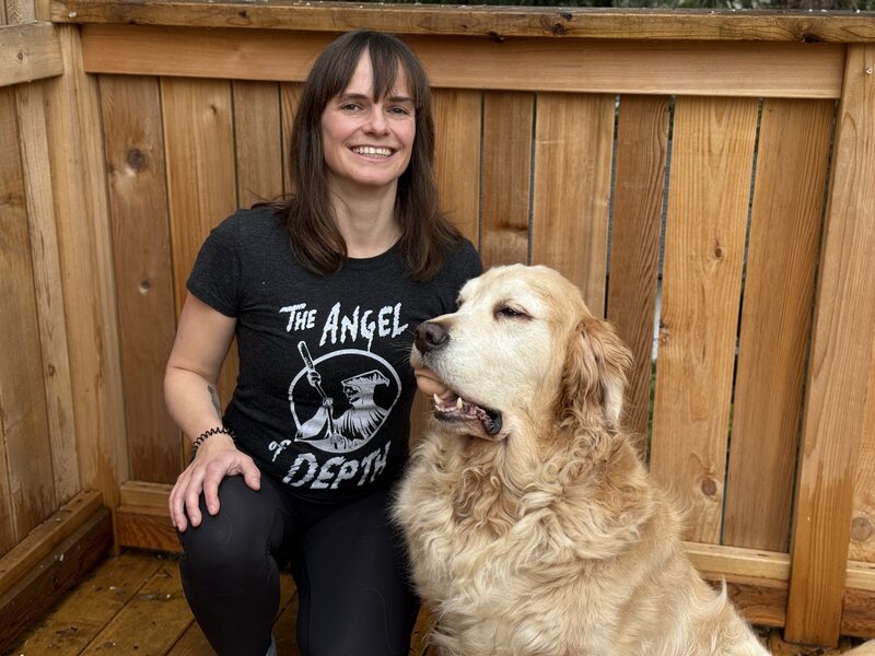 Connie smiling beside a golden retriever